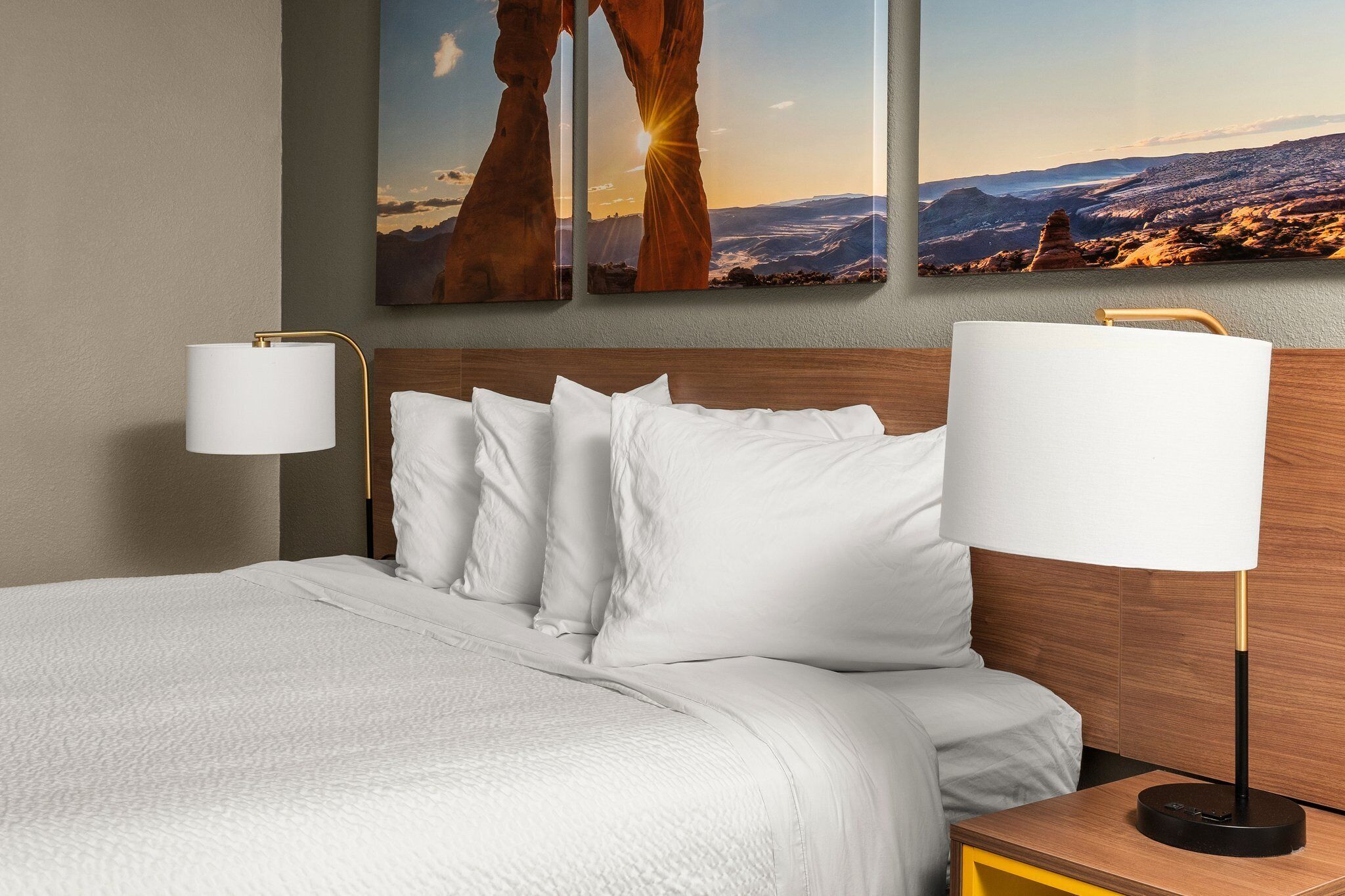 Habitación de hotel con una cama grande, dos lámparas fijadas a la pared y dos cuadros con paisajes.