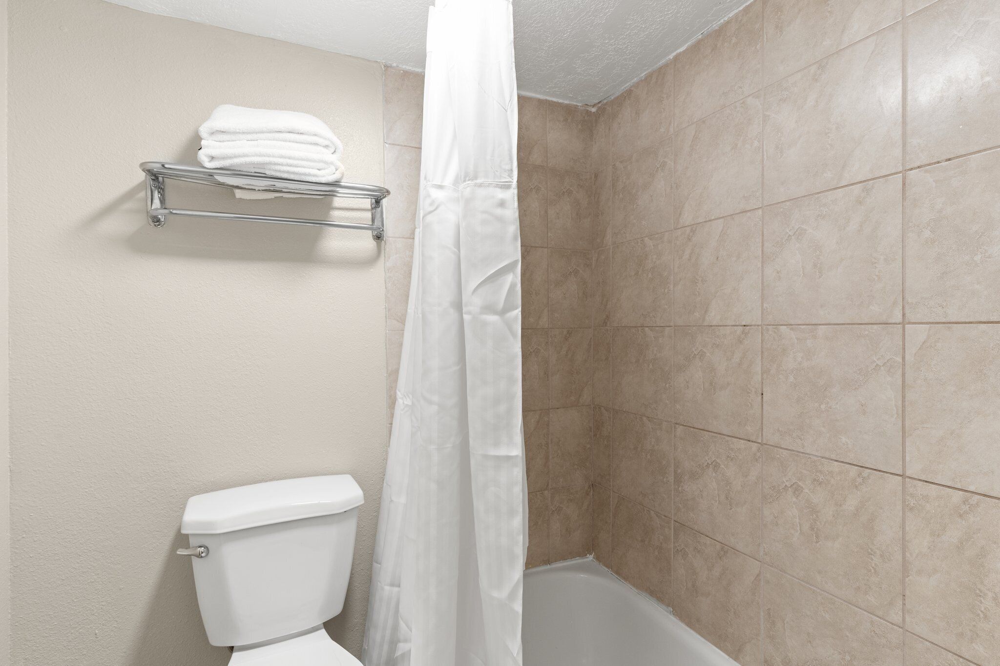 Un baño con inodoro, ducha con cortina blanca y toallero con toallas dobladas.