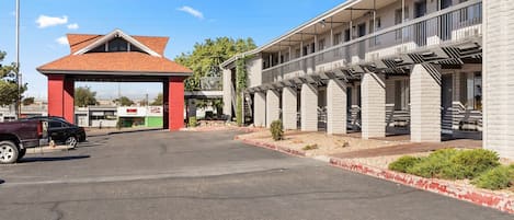 A motel with a red entrance archway, a parking lot, and a row of rooms with balconies.