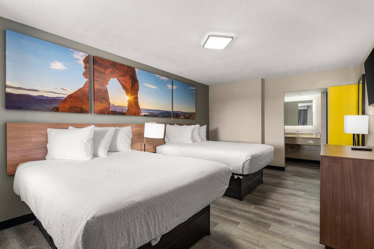Ein Hotelzimmer mit zwei Betten, einem großen Wandgemälde, einem Spiegel und einem Schreibtisch mit Lampe.
