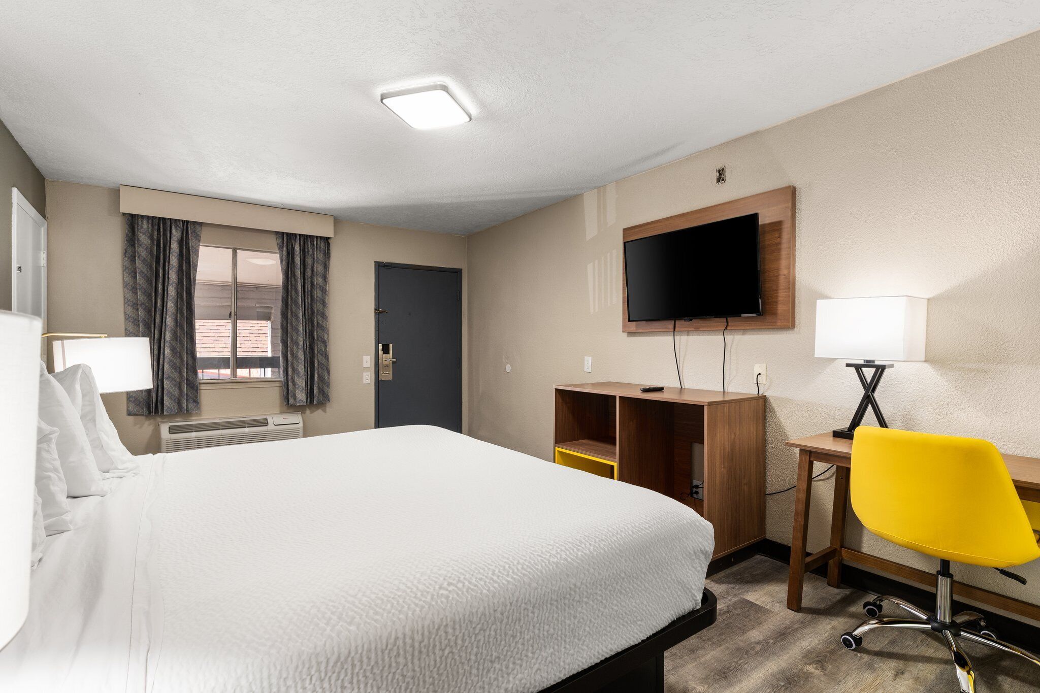 A hotel room with a large bed, a desk with a chair, a television, and a window with curtains.