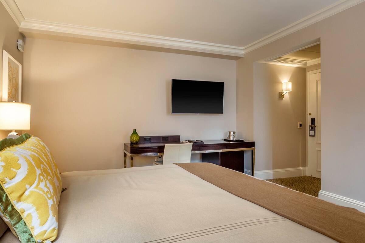 Quarto de hotel com cama, escrivaninha, cadeira, televisão de tela plana e abajur.