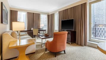 A hotel room with a sofa, armchair, TV, and a balcony with a wrought iron railing.