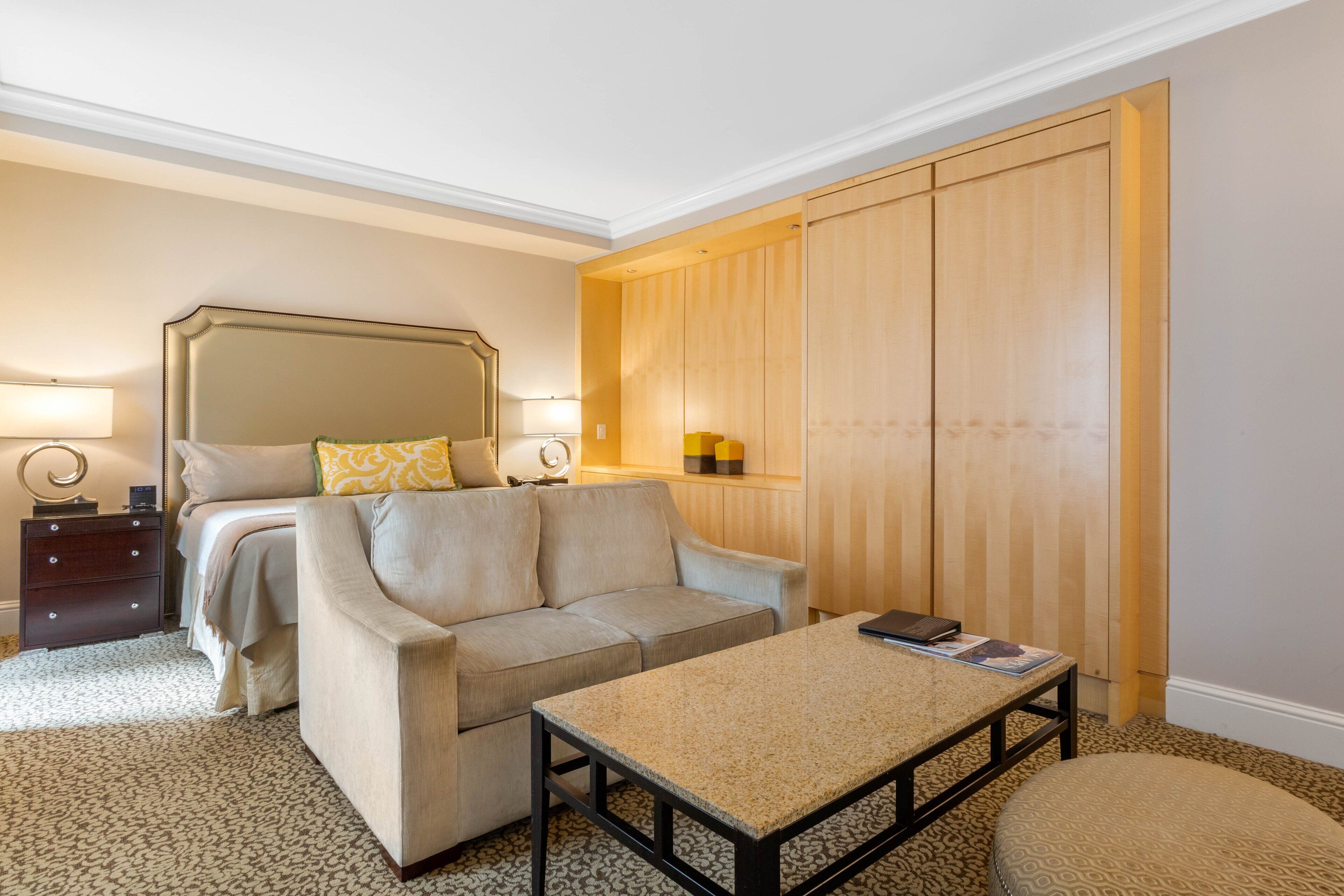 A hotel room with a bed, a sofa, a coffee table, a nightstand, and a wardrobe.