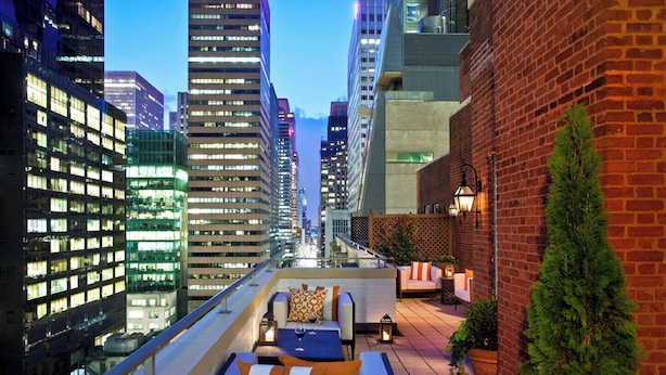 A rooftop terrace with outdoor seating, a brick wall, and a view of city buildings.