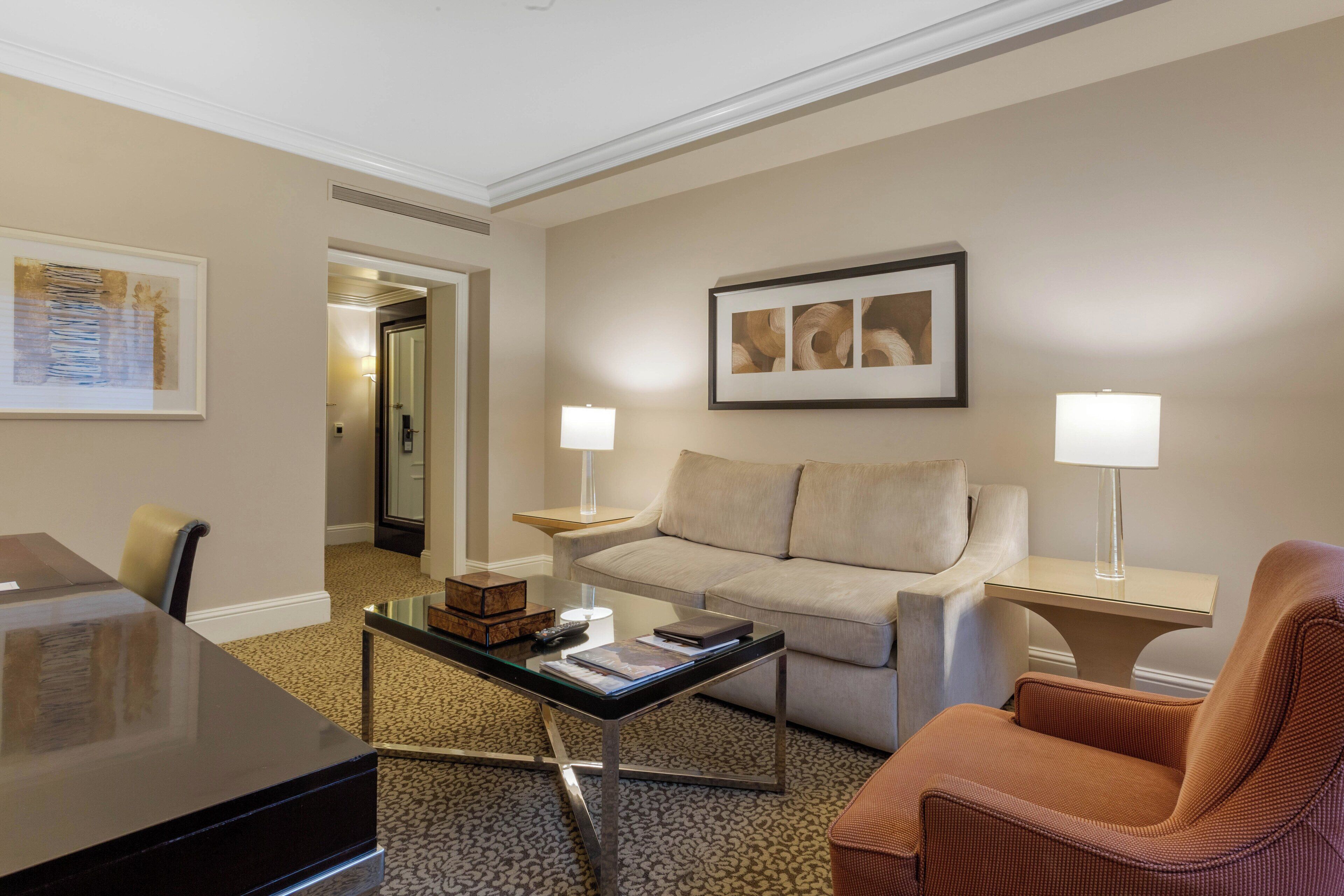 Una sala de estar moderna con una mesa de centro de vidrio, un sofá, un sillón y un escritorio con una lámpara.