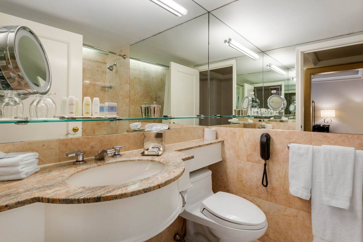 Um banheiro moderno com pia de mármore, box de vidro, vaso sanitário branco e um espelho grande.