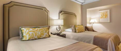 A hotel room with two beds, each with a headboard, a bedside table with a lamp, and a framed artwork on the wall.