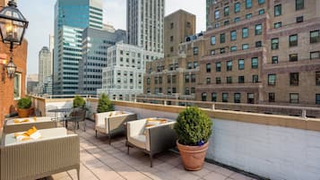 Terraza en la azotea con mobiliario de mimbre, plantas en macetas y vistas panorámicas de la ciudad.