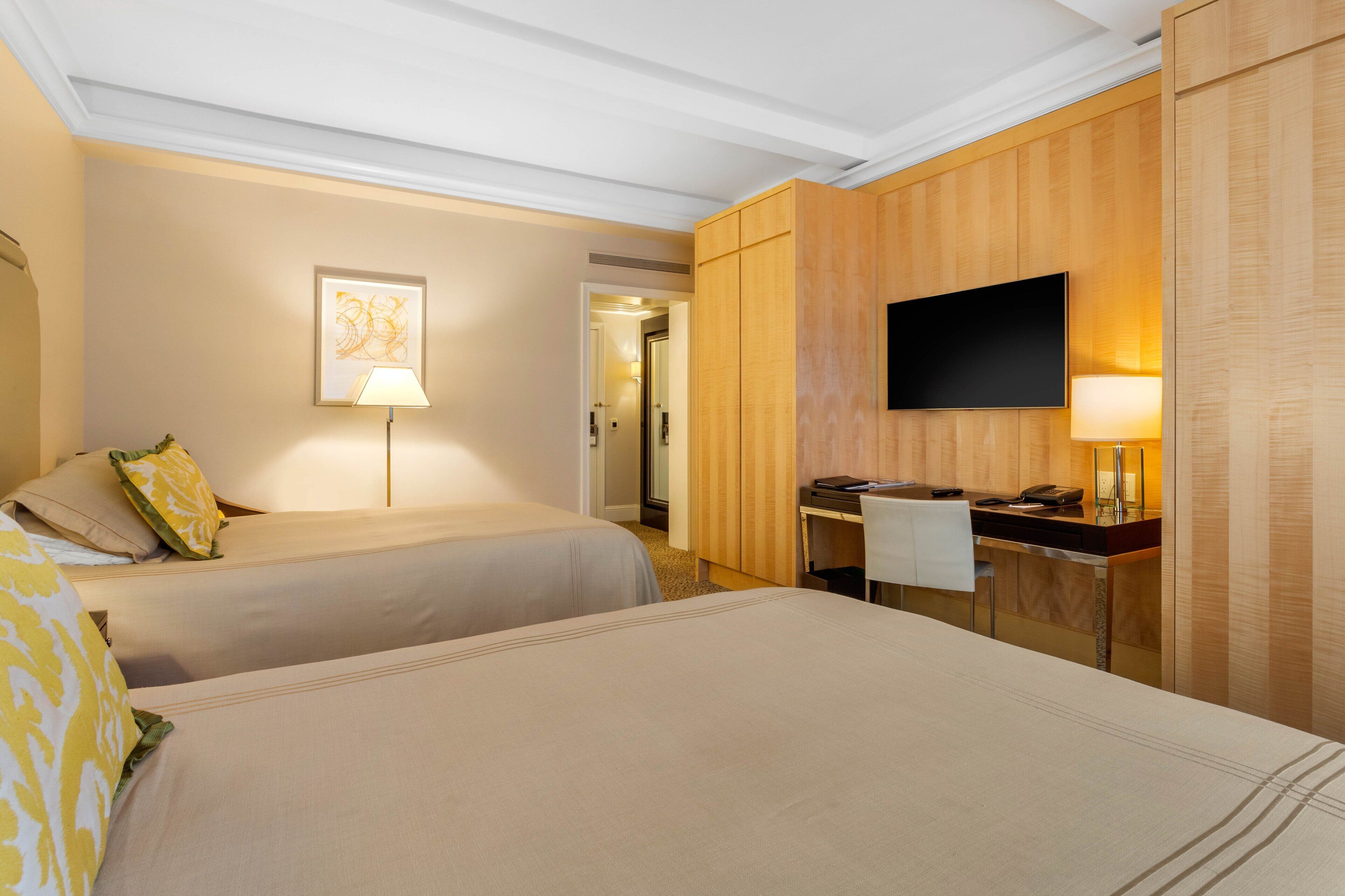 A hotel room with two beds, a desk, a flat-screen TV, and a framed picture on the wall.