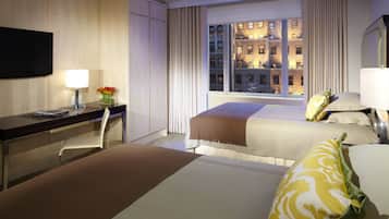 A hotel room with two beds, a desk, a chair, a TV, and a window with a city view.
