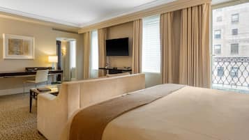 Une chambre d’hôtel dotée d’un grand lit, d’un bureau avec une chaise, d’un téléviseur à écran plat fixé au mur et d’un balcon offrant une vue sur la ville.