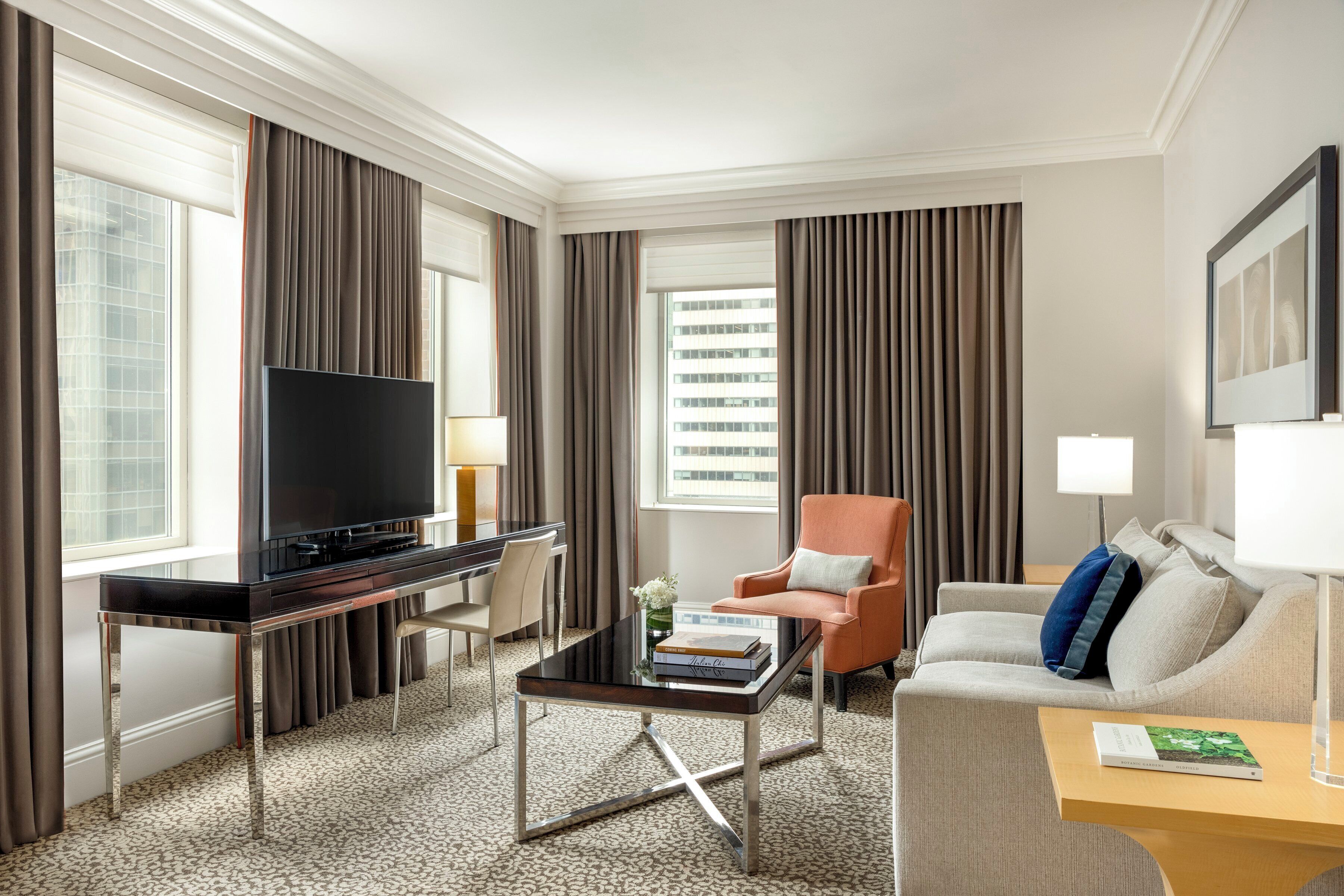 Une chambre d’hôtel équipée d’une télévision à écran plat, d’un canapé, d’un fauteuil, d’une table basse et d’un bureau.