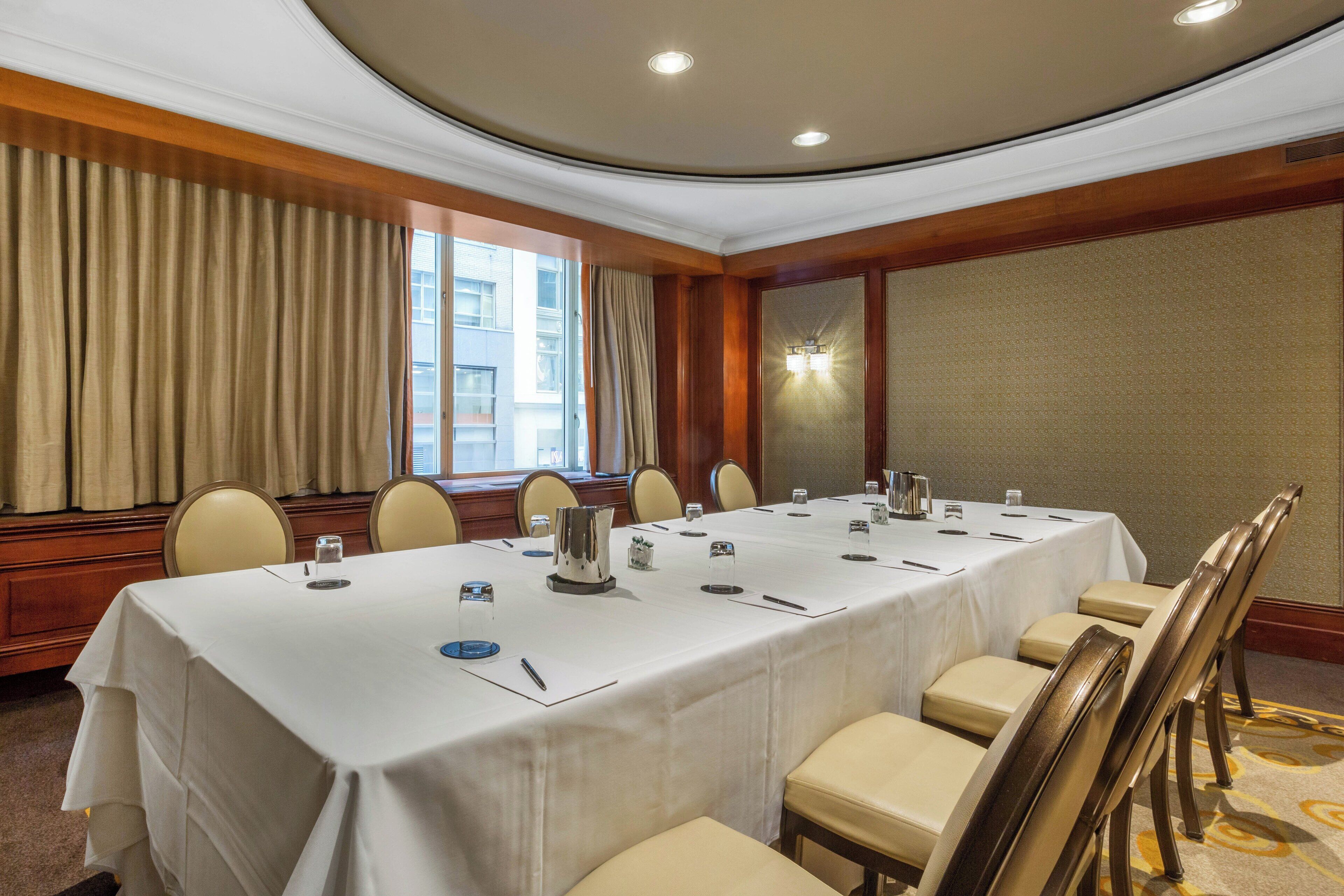 A conference room with a long table, chairs, and a window with curtains.