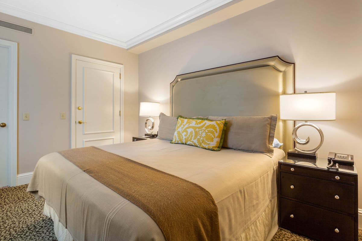 Una habitación de hotel ordenada con una cama grande, dos mesitas de noche y una puerta.