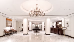 A spacious lobby with a grand chandelier, marble flooring, and a reception desk.
