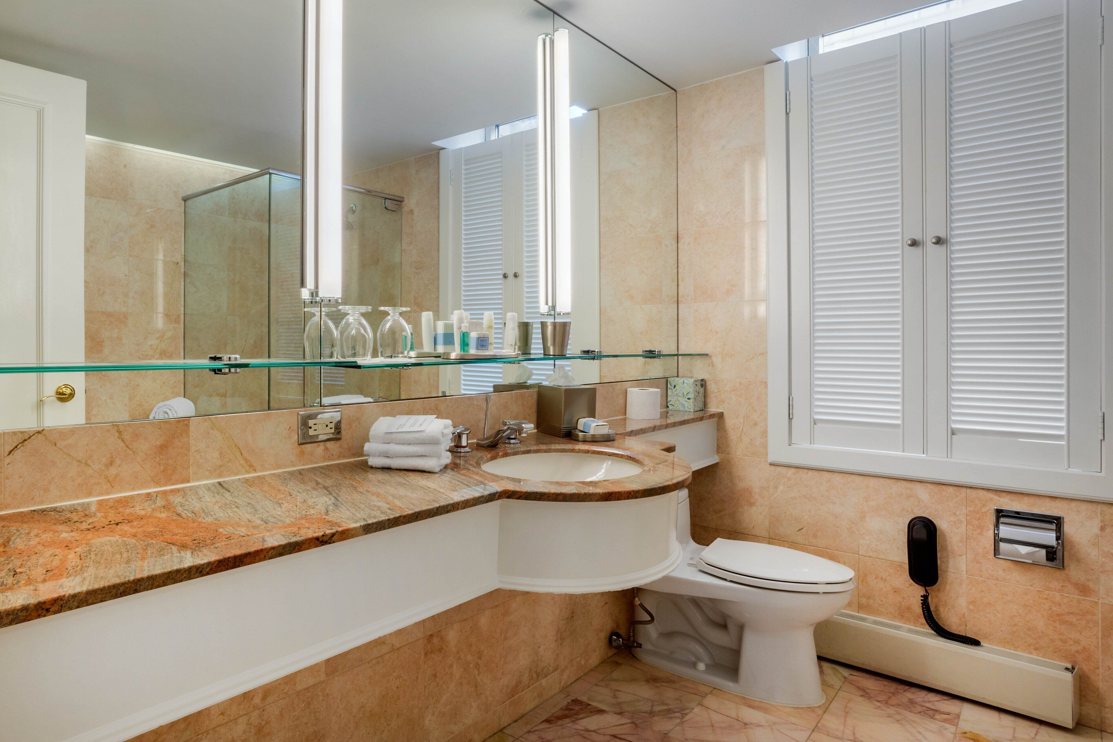 A modern bathroom with a glass shower enclosure, a marble countertop, a toilet, and a telephone.