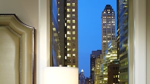 A hotel room with a large window offering a view of a cityscape at dusk.