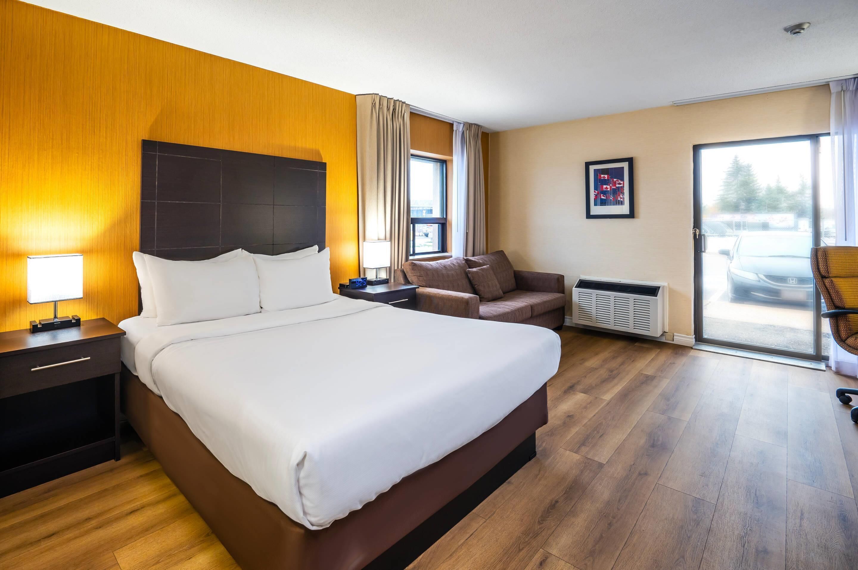 A hotel room with a large bed, a nightstand, a chair, and a view of the outside through a sliding door.