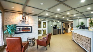 A hotel lobby with a reception desk, two leather chairs, a stone wall with a fireplace, and a sign that reads "Quality by Choice Hotels." - Quality Inn (Barrie)