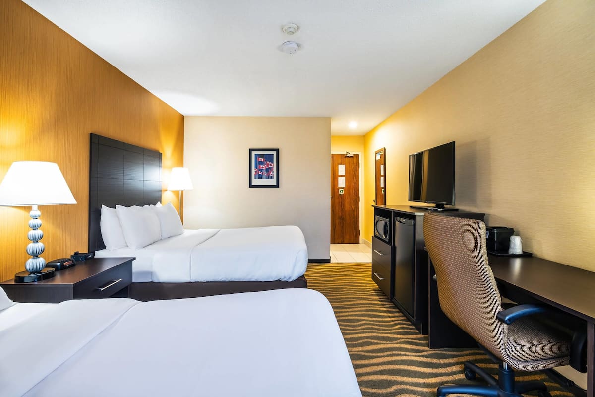 A hotel room with two beds, a desk with a chair, a television, and a lamp.