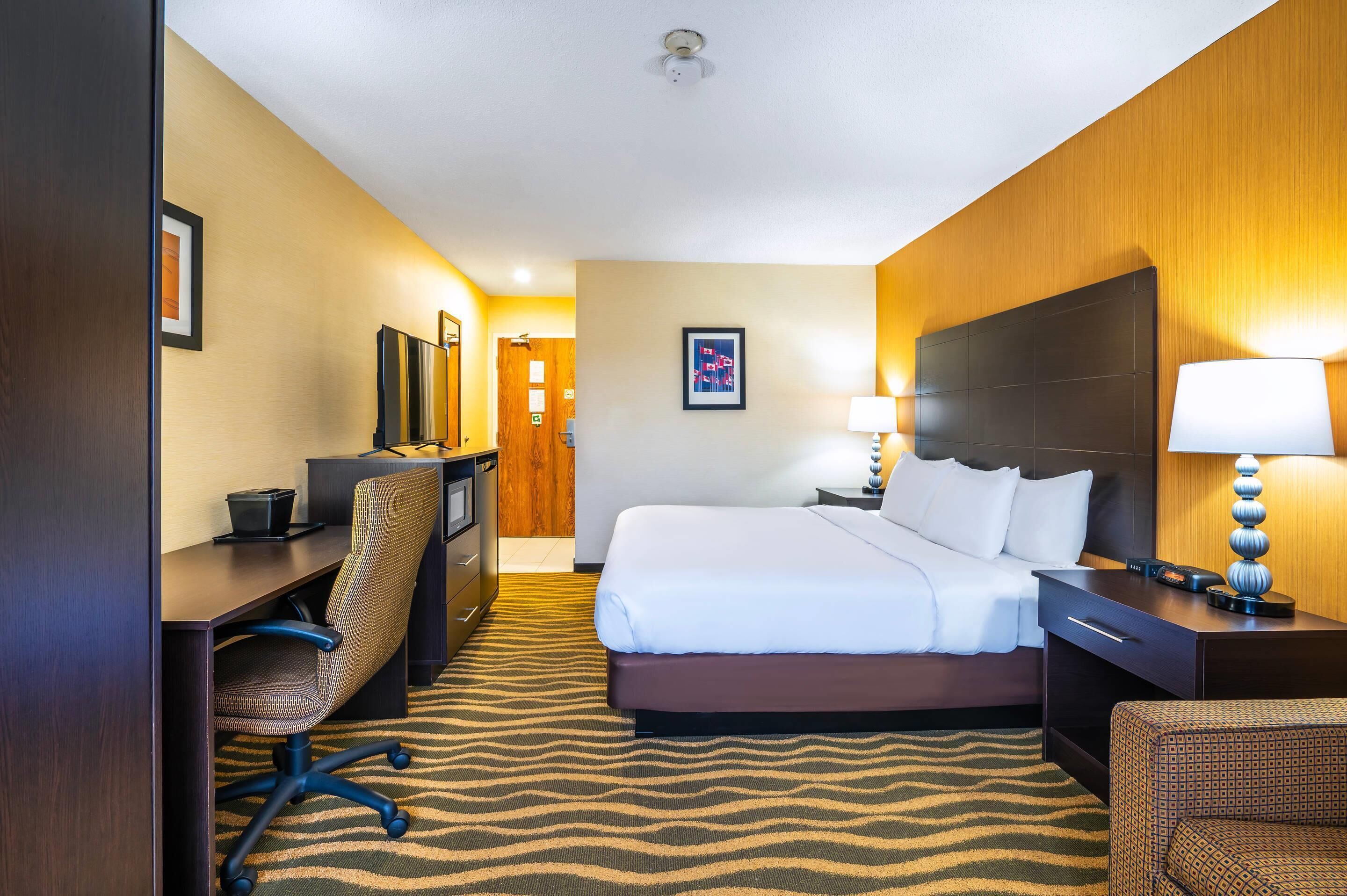A hotel room with a bed, desk, chair, and a television.