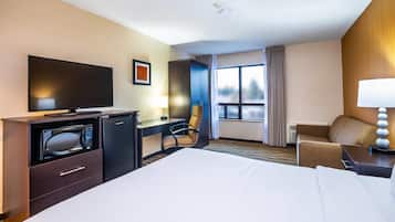 Habitación de hotel con cama, escritorio con televisor de pantalla plana, microondas, silla, sofá y ventana con cortinas.