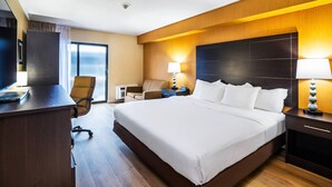 A hotel room with a large bed, a desk, a chair, a TV, and a lamp. - Quality Inn (Barrie)