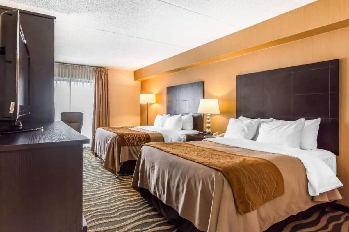A hotel room with two beds, a desk, a television, and a window with curtains.