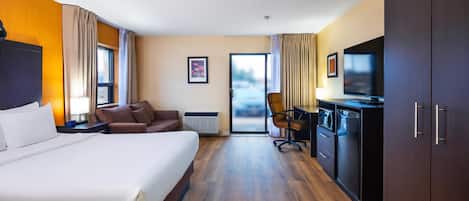 A hotel room with a large bed, a desk with a chair, a TV, a wardrobe, and a sliding door to the outside.