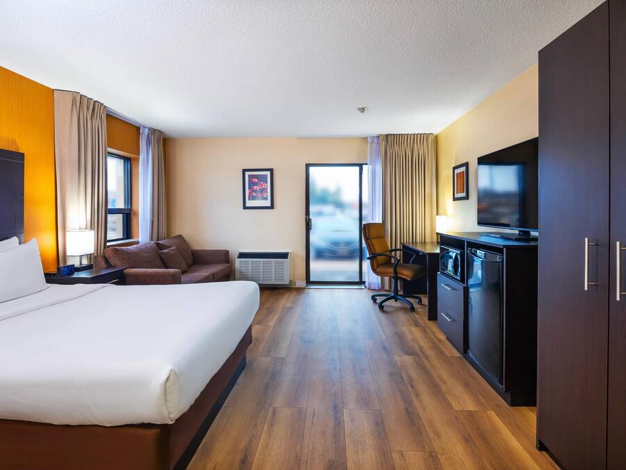 A hotel room with a large bed, a desk with a chair, a TV, a wardrobe, and a sliding door to the outside.
