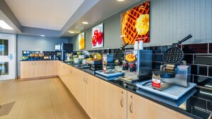 A modern kitchen with a long counter, waffle maker, and various cooking appliances. - Quality Inn (Barrie)