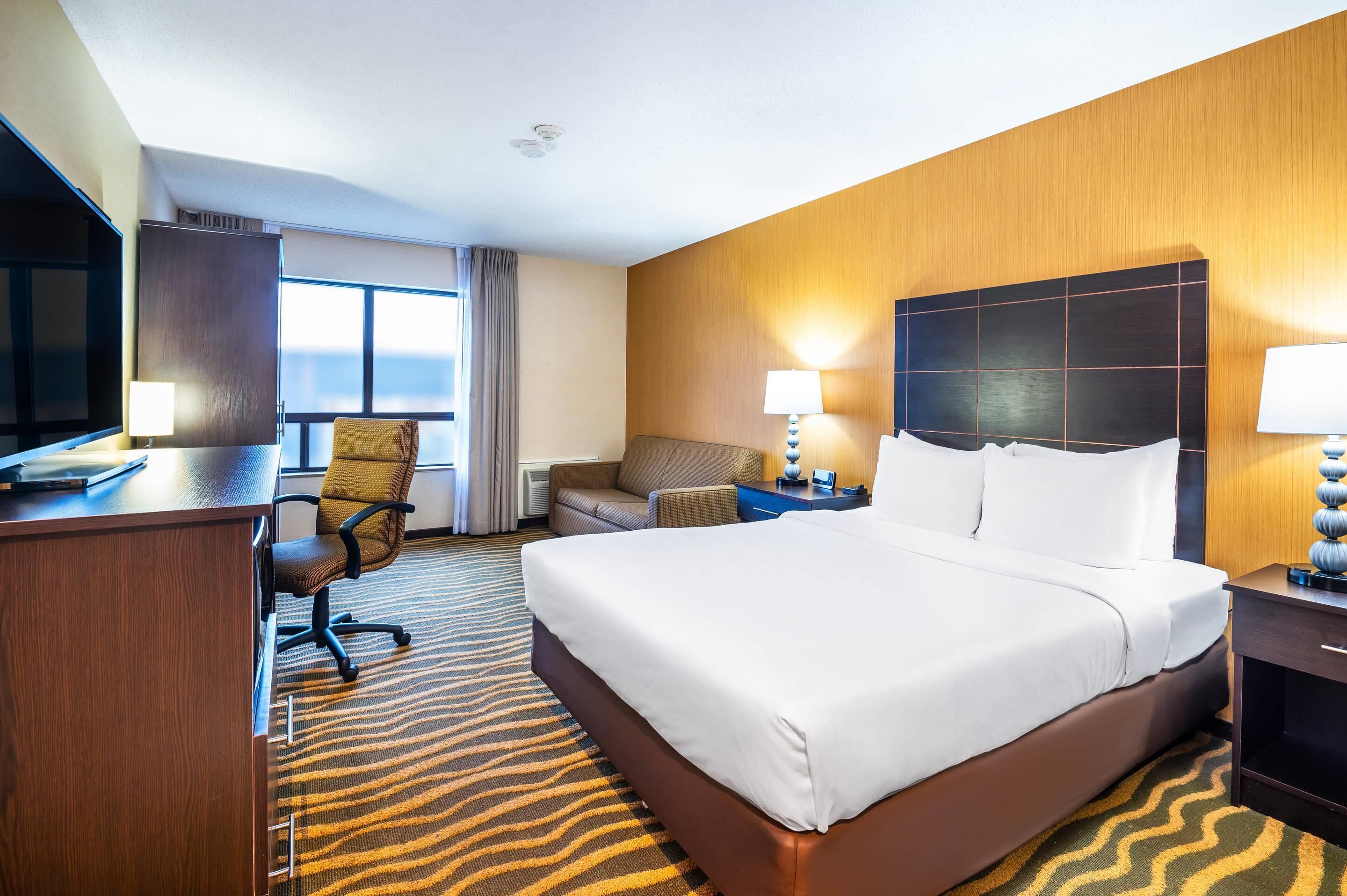 A hotel room with a large bed, a desk, a chair, a sofa, and a television.