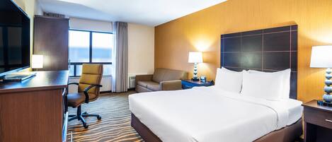 A hotel room with a large bed, a desk, a chair, a sofa, and a television.