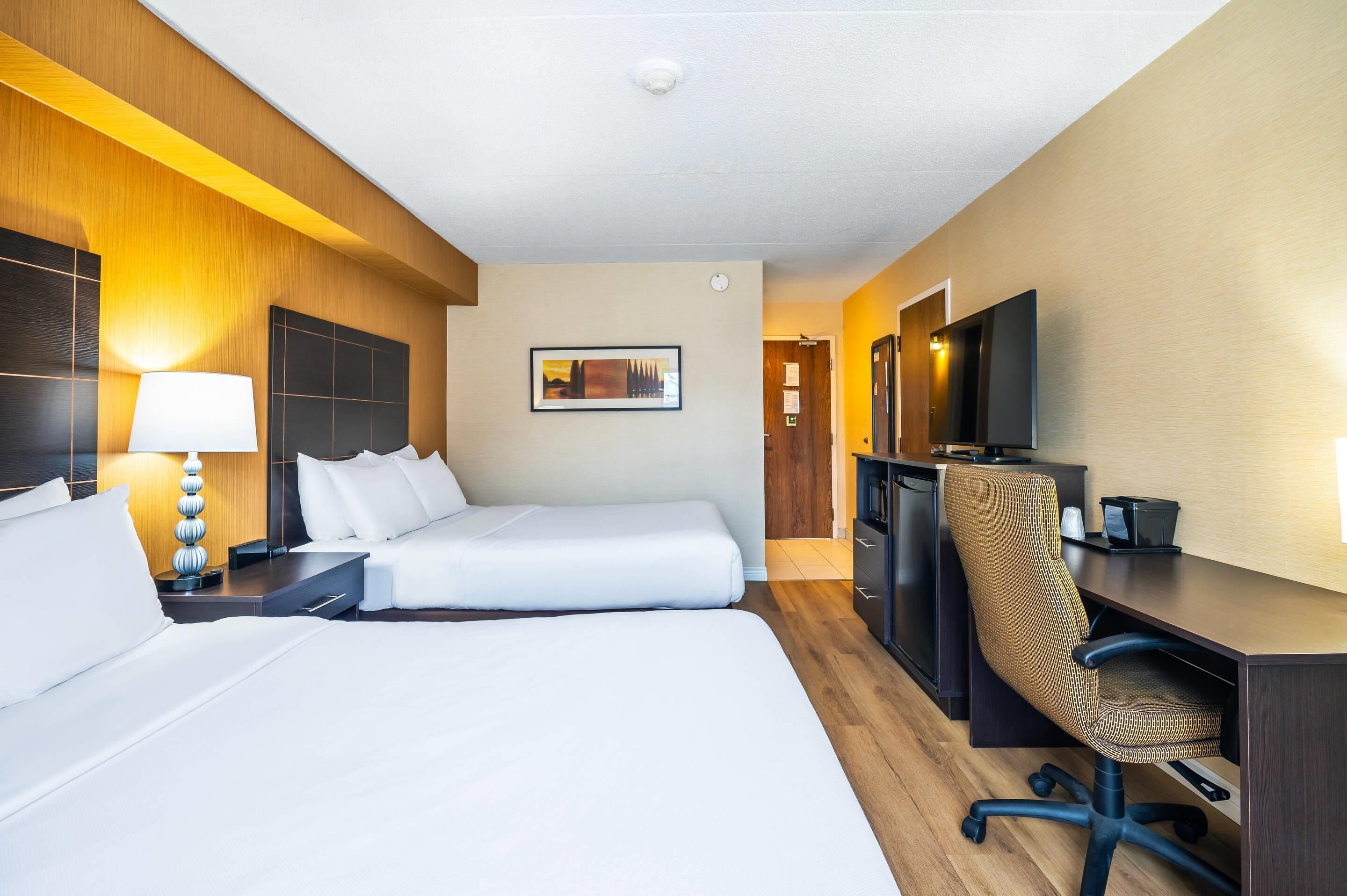 Habitación de hotel con dos camas, un escritorio, una silla, un televisor y una lámpara.