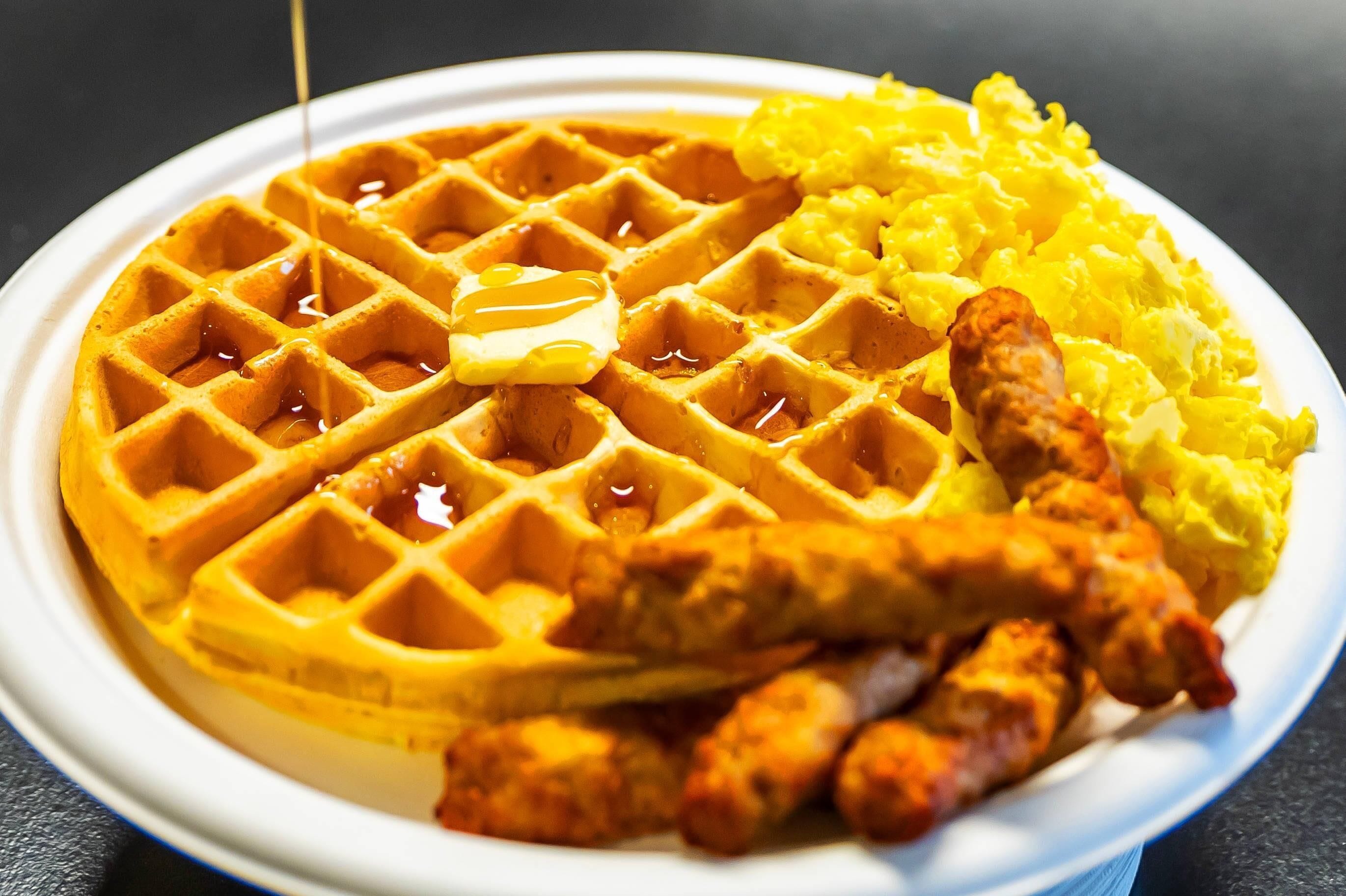 A plate with a waffle, scrambled eggs, and sausage.