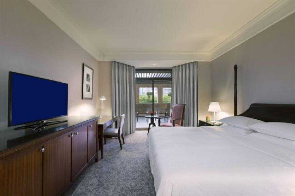 Habitación de hotel con cama, televisor, escritorio y una silla. Cuenta con un balcón con mesa y sillas.