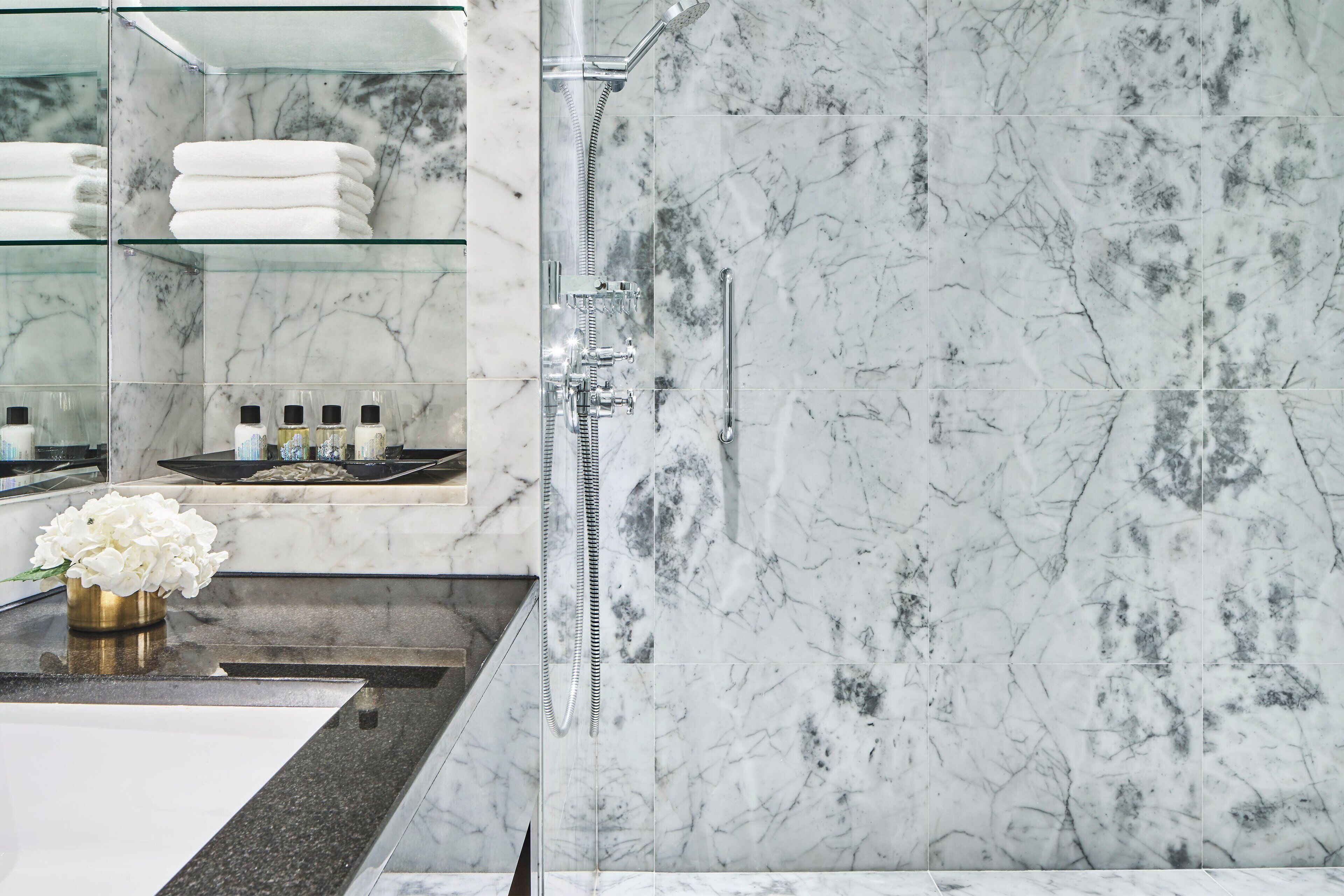 A modern bathroom with a marble shower, a glass-topped sink, and neatly folded towels.
