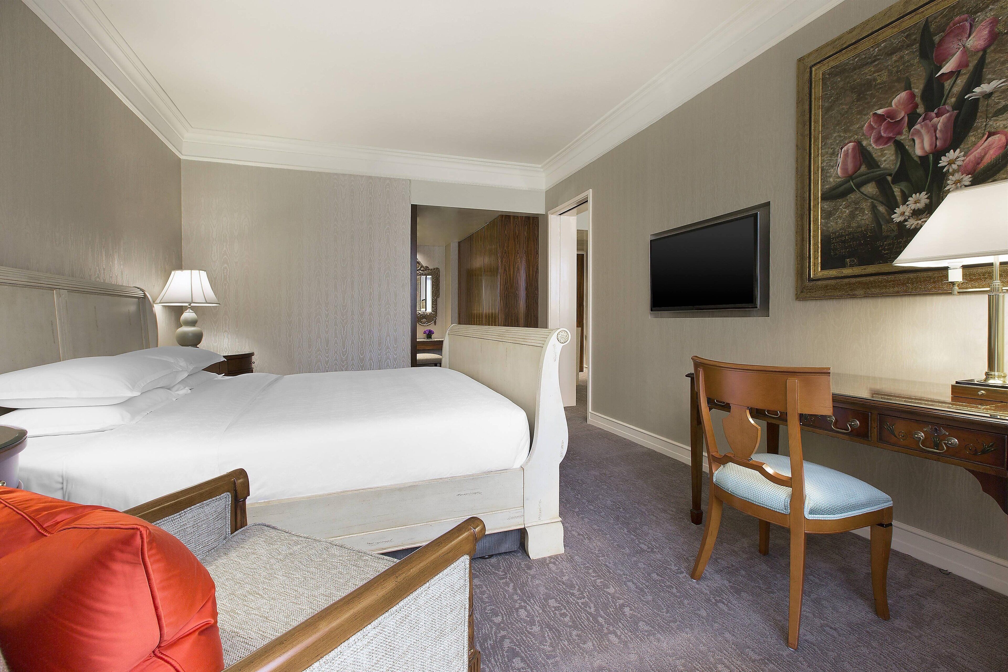 Een hotelkamer met een groot bed, een bureau met een lamp, een stoel en een schilderij aan de muur.