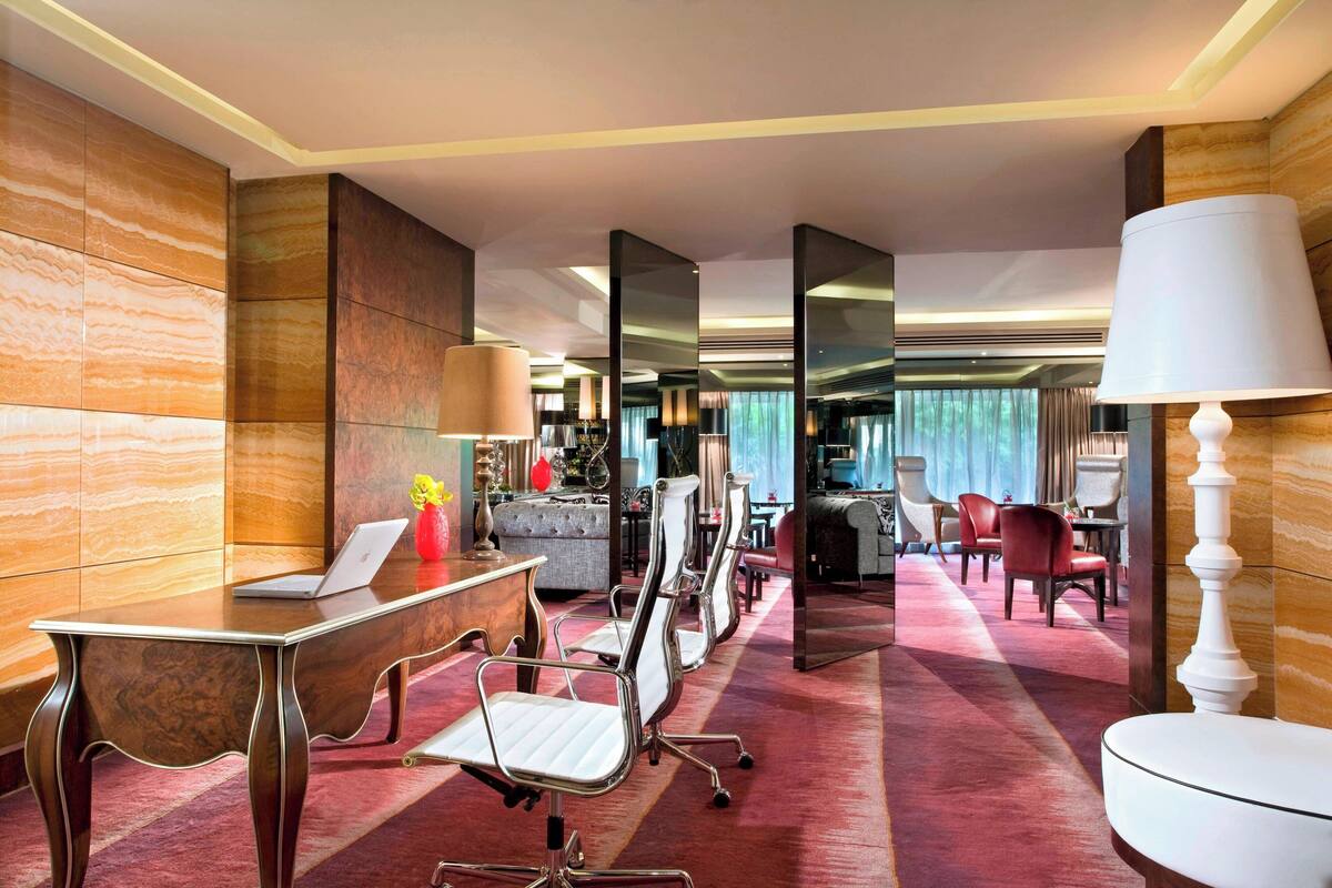 Un hall de hotel con mostrador de recepción, sillas modernas, alfombra roja y vistas al comedor.