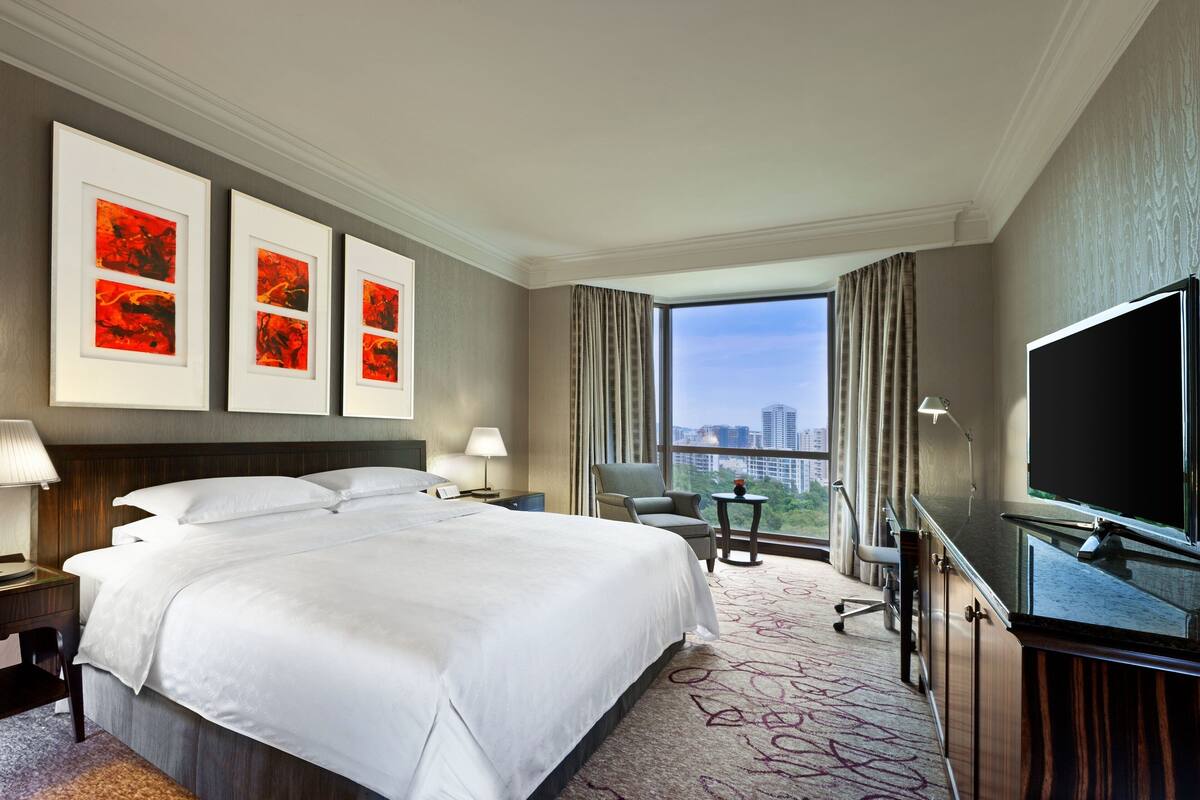 Habitación de hotel con una cama grande, un escritorio con silla, un televisor y vistas a la ciudad.