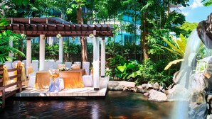 Un entorno tranquilo al aire libre con una pérgola de madera, asientos blancos acolchados y un estanque de carpas.