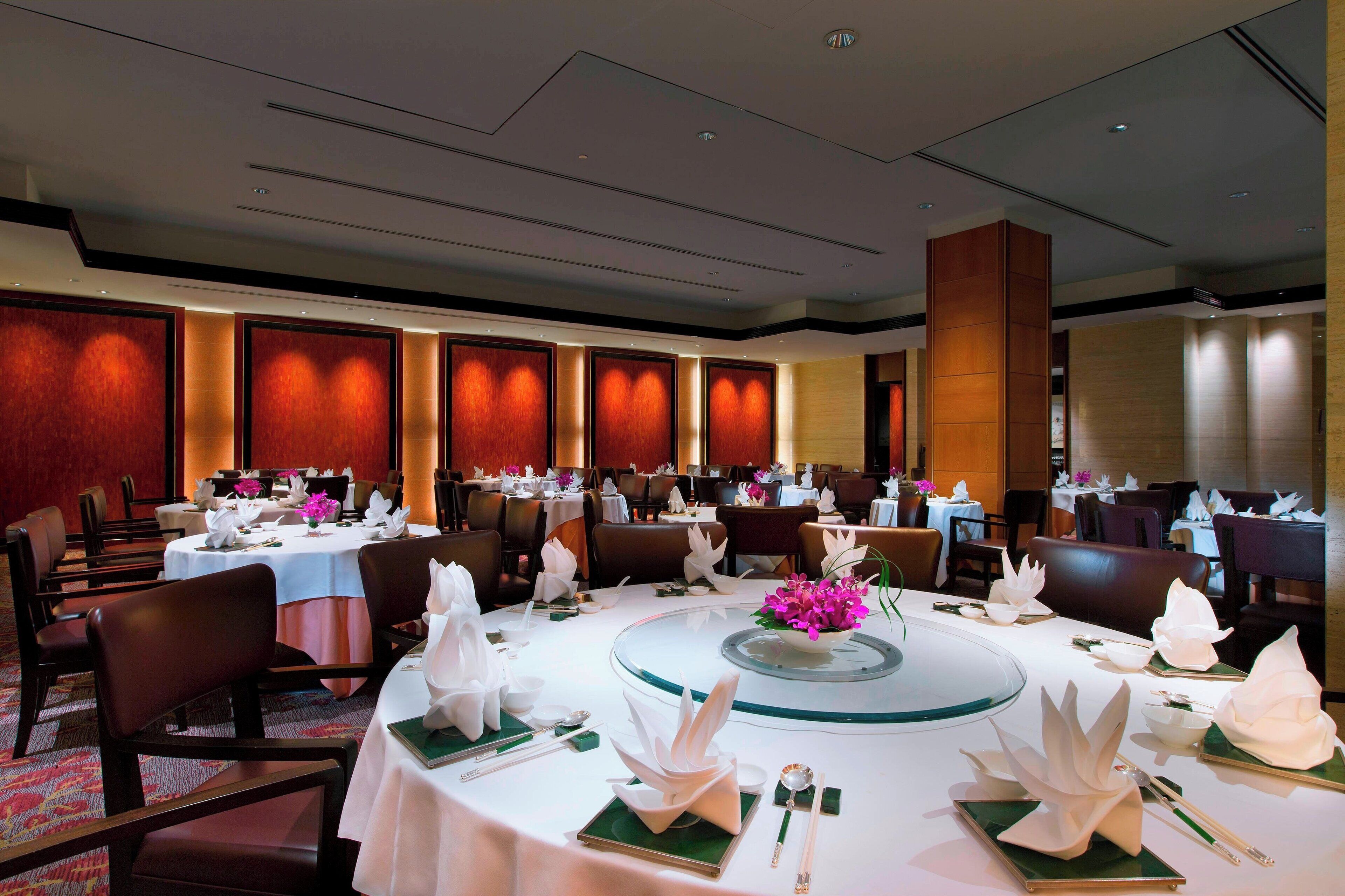 A banquet hall with round tables set for dining, featuring white tablecloths, green placemats, and floral centerpieces.