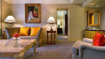 Una habitación de hotel con sofá, sillón, mesa, lámparas, un cuadro y un espejo.