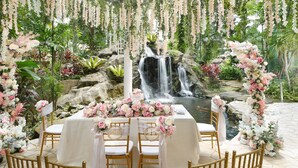 Montaje de recepción de bodas con cascada de fondo, decoración floral y piso de baldosas de piedra.