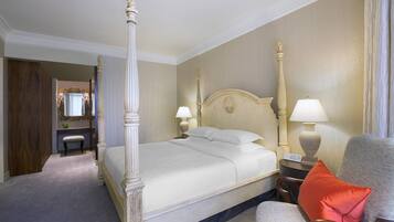 Un lit à baldaquin avec une tête de lit, des lampes de chevet, une chaise avec un coussin rouge et une petite table avec une lampe.
