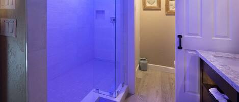 Een moderne badkamer met een douchecabine van glas, een houten wastafelmeubel en een deur naar een andere kamer.