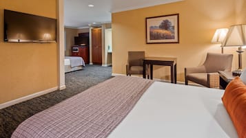Een hotelkamer met een groot bed, een televisie, een bureau, een stoel en een schilderij aan de muur.