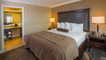 A hotel room with a large bed, two bedside lamps, a nightstand, a chair, and a bathroom visible through an open door.
