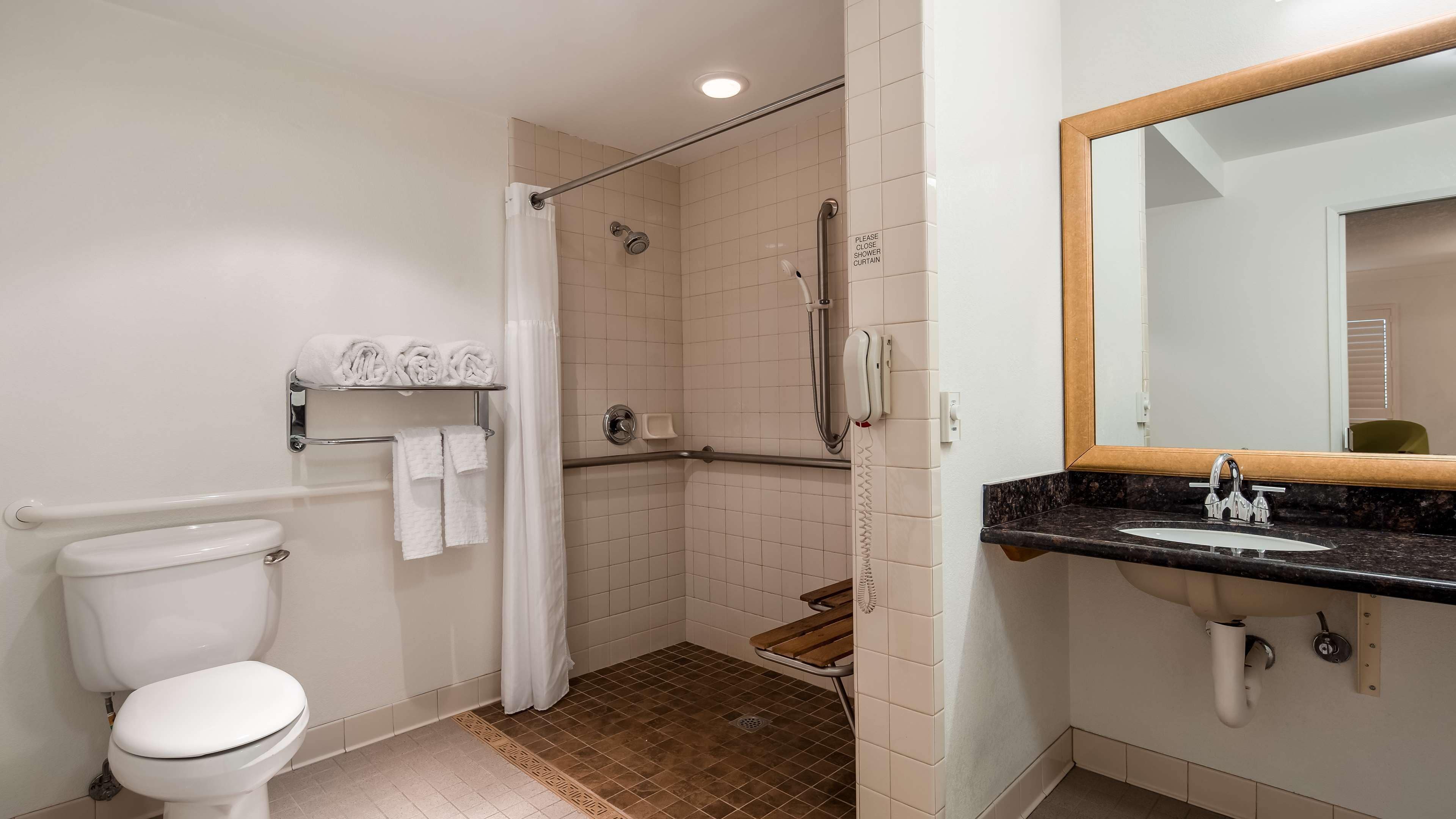 A bathroom with a toilet, a shower with a glass door, a sink with a mirror, and a towel rack with folded towels.